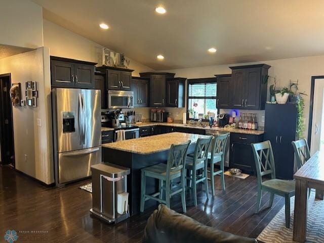 959 29th Ave W, West Fargo, ND 58078 - kitchen with appliances with stainless steel finishes, a kitchen island, vaulted ceiling, dark wood-style flooring, and a kitchen breakfast bar