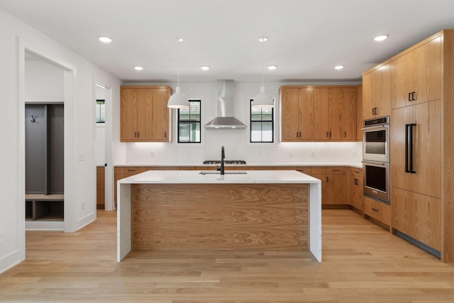 2084 Palace Ave, Saint Paul, MN 55105 - kitchen with wall chimney range hood, stainless steel double oven, light wood-type flooring, a kitchen island with sink, and hanging light fixtures