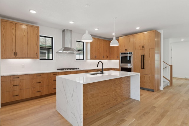 2084 Palace Ave, Saint Paul, MN 55105 - kitchen featuring wall chimney exhaust hood, stainless steel double oven, gas cooktop, light wood finished floors, and a kitchen island with sink