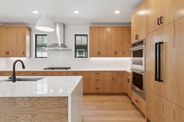 2084 Palace Ave, Saint Paul, MN 55105 - kitchen featuring wall chimney range hood, stainless steel appliances, decorative light fixtures, backsplash, and light wood-style floors