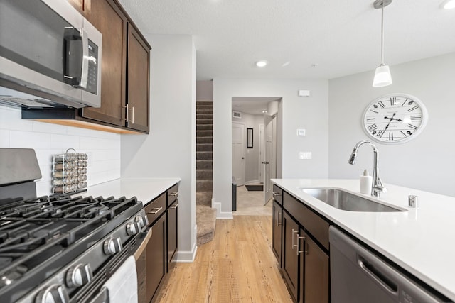 7237 Ada Dr, Lino Lakes, MN 55038 - kitchen with stainless steel appliances, light countertops, light wood finished floors, dark brown cabinets, and hanging light fixtures