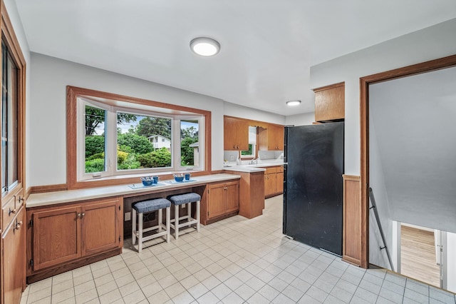6781 Plaza Curv NE, Fridley, MN 55432 - kitchen featuring freestanding refrigerator, light countertops, brown cabinetry, built in desk, and light tile patterned flooring