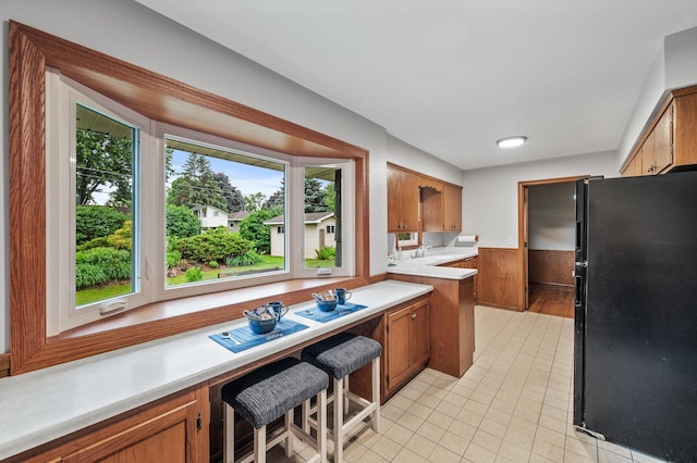 6781 Plaza Curv NE, Fridley, MN 55432 - kitchen featuring freestanding refrigerator, healthy amount of natural light, brown cabinetry, light countertops, and wainscoting