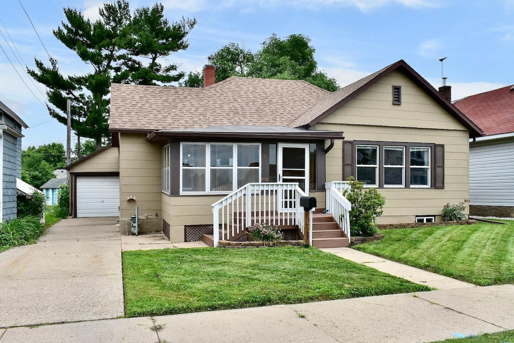 663 Wilson St, Winona, MN 55987 - bungalow featuring a chimney, roof with shingles, concrete driveway, a garage, and a front yard