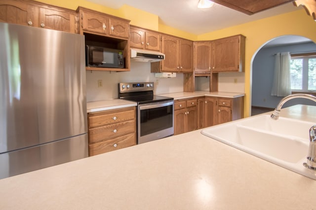 12423 93rd Ave N, Maple Grove, MN 55369 - kitchen with stainless steel appliances, under cabinet range hood, brown cabinetry, and arched walkways