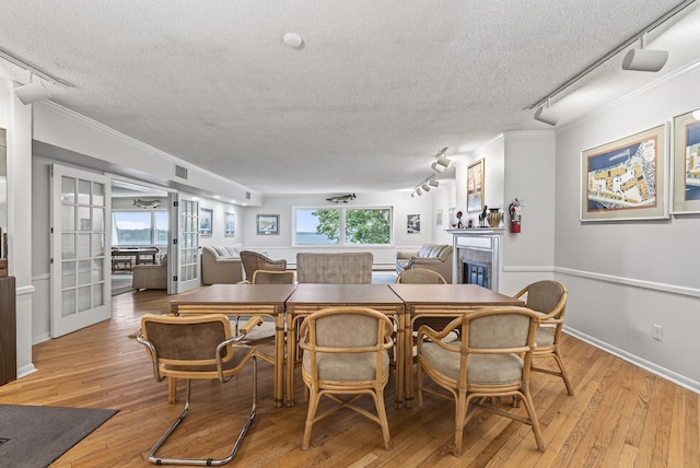 4371 Wilshire Blvd Unit 107, Mound, MN 55364 - dining space featuring a textured ceiling, track lighting, light wood-style flooring, ornamental molding, and a glass covered fireplace