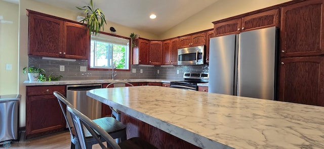 961 39 1/2 Ave W, West Fargo, ND 58078 - kitchen featuring stainless steel appliances, lofted ceiling, light countertops, decorative backsplash, and a kitchen breakfast bar