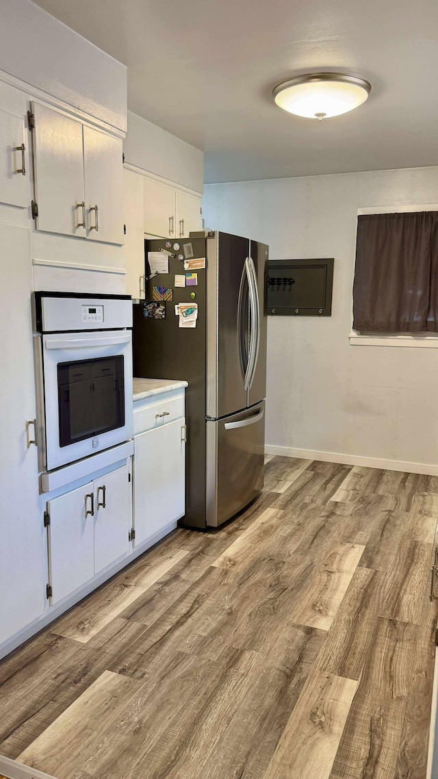 306 4th St, La Crescent, MN 55947 - kitchen with white oven, freestanding refrigerator, wood finished floors, white cabinetry, and light countertops