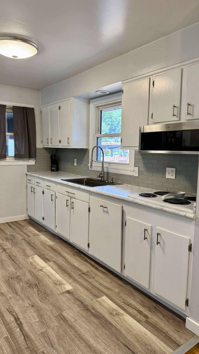306 4th St, La Crescent, MN 55947 - kitchen with white electric cooktop, white cabinets, decorative backsplash, light wood-type flooring, and light countertops