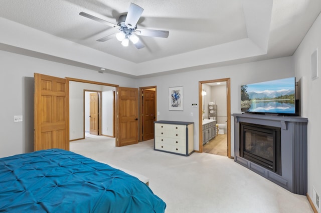 13756 Skyline Cir, Louisville Twp, MN 55379 - bedroom featuring a glass covered fireplace, ensuite bathroom, light colored carpet, ceiling fan, and a tray ceiling