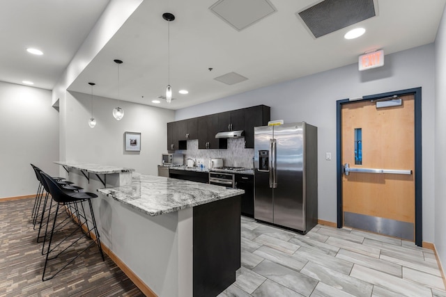 740 Portland Ave Unit 801, Minneapolis, MN 55415 - kitchen featuring stainless steel appliances, a kitchen breakfast bar, dark cabinetry, decorative backsplash, and under cabinet range hood