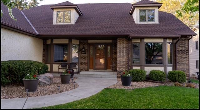 469 Lake Wabasso Ct, Shoreview, MN 55126 - doorway to property featuring brick siding, a porch, roof with shingles, and a lawn