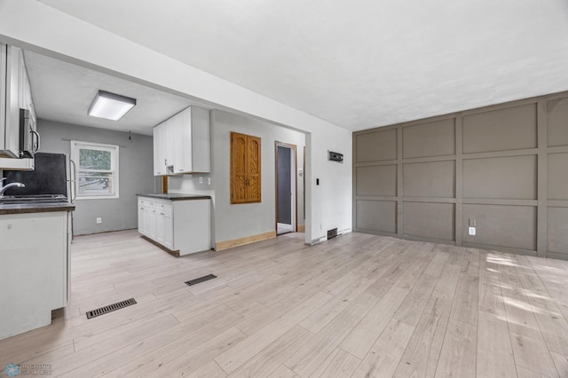 1130 Oak St N, Fargo, ND 58102 - kitchen featuring dark countertops, light wood-type flooring, white cabinets, stainless steel microwave, and a decorative wall