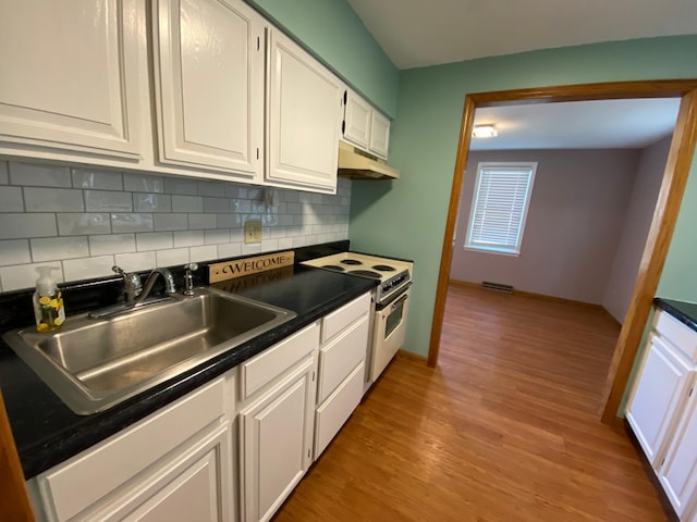 108 20th St S, Benson, MN 56215 - kitchen featuring white range with electric stovetop, under cabinet range hood, dark countertops, white cabinetry, and decorative backsplash