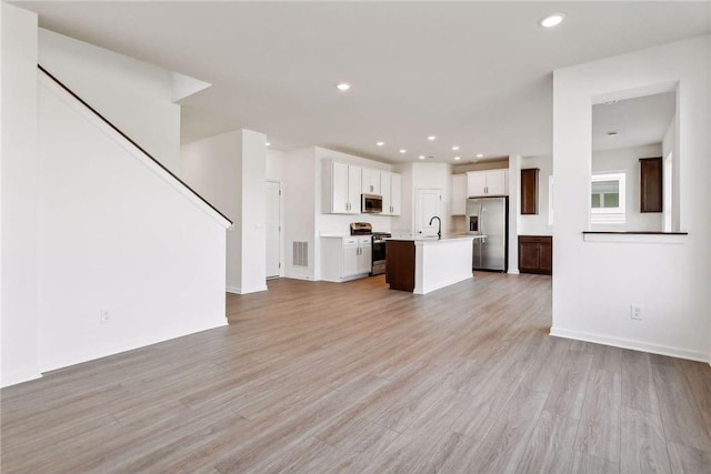 unfurnished living room featuring light wood-style flooring, recessed lighting, and stairway