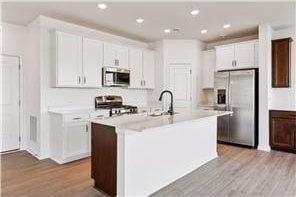 kitchen featuring stainless steel appliances, wood finished floors, light countertops, white cabinets, and a center island with sink