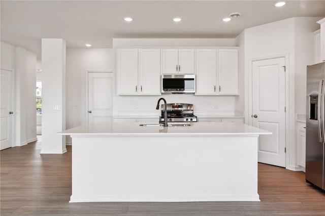 kitchen with appliances with stainless steel finishes, a center island with sink, light countertops, wood finished floors, and recessed lighting