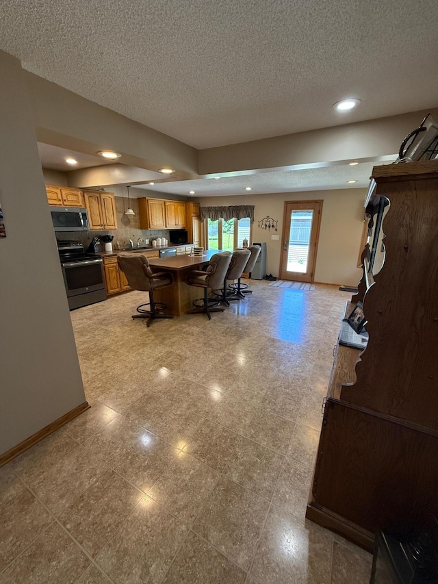 411 Vernon Ave, Morgan, MN 56266 - kitchen with appliances with stainless steel finishes, a textured ceiling, brown cabinets, a breakfast bar area, and recessed lighting