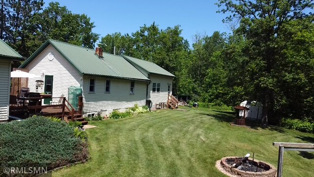 37452 Deer St, Aitkin, MN 56431 - rear view of house with an outdoor fire pit, a lawn, a wooden deck, a metal roof, and a chimney