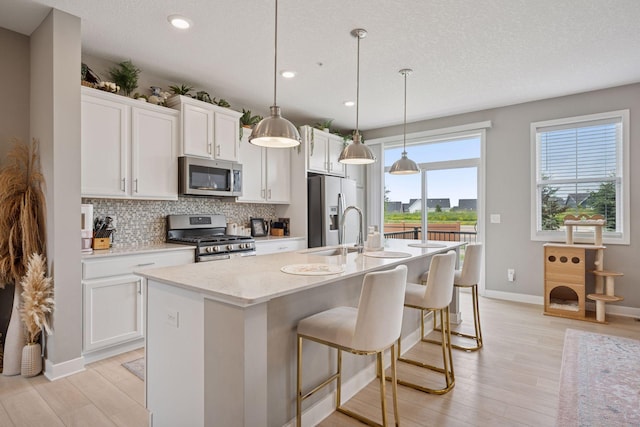18874 72nd Pl N, Maple Grove, MN 55311 - kitchen with stainless steel appliances, an island with sink, backsplash, light wood finished floors, and white cabinetry