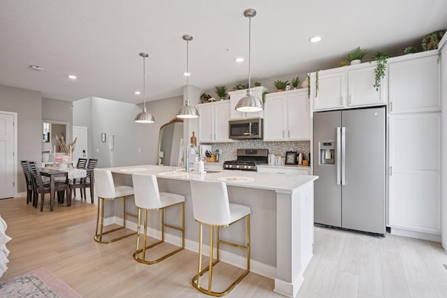 18874 72nd Pl N, Maple Grove, MN 55311 - kitchen with appliances with stainless steel finishes, a center island with sink, tasteful backsplash, light wood-type flooring, and a breakfast bar area