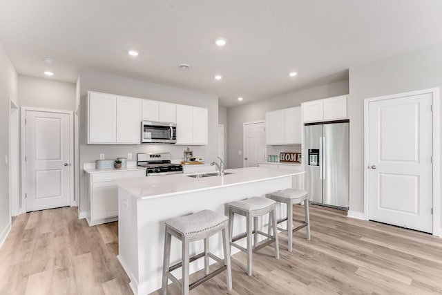 12691 Fraizer St NE, Blaine, MN 55449 - kitchen featuring stainless steel appliances, light wood finished floors, a kitchen island with sink, a kitchen bar, and light countertops