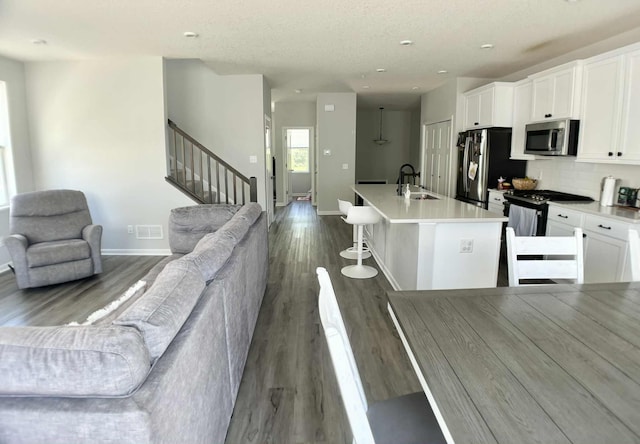 7628 Carla Path, Inver Grove Heights, MN 55076 - kitchen featuring appliances with stainless steel finishes, open floor plan, white cabinets, an island with sink, and dark wood-style floors
