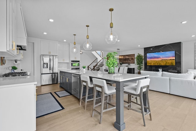 9612 Iron Horse Rd, Woodbury, MN 55129 - kitchen with stainless steel appliances, white cabinetry, light wood finished floors, recessed lighting, and light countertops