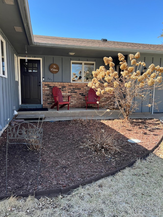 301 Nottingham Ct, North Mankato, MN 56003 - doorway to property featuring board and batten siding, brick siding, a porch, and roof with shingles