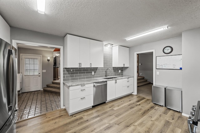11542 Xavis St NW, Coon Rapids, MN 55433 - kitchen featuring stainless steel appliances, light wood finished floors, a textured ceiling, tasteful backsplash, and white cabinets