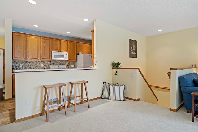 1112 Iris Dr, White Bear Twp, MN 55127 - kitchen with white appliances, a breakfast bar area, decorative backsplash, light colored carpet, and recessed lighting