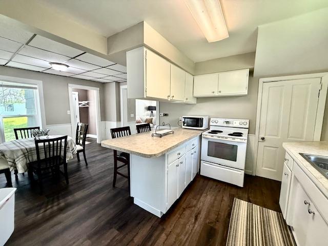 311 Grove St, Redwood Falls, MN 56283 - kitchen featuring white range with electric stovetop, light countertops, a peninsula, white cabinetry, and a breakfast bar area