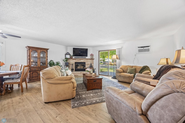 2575 Pacific Dr S Unit 301, Fargo, ND 58103 - living room with an AC wall unit, light wood finished floors, a ceiling fan, a textured ceiling, and a glass covered fireplace