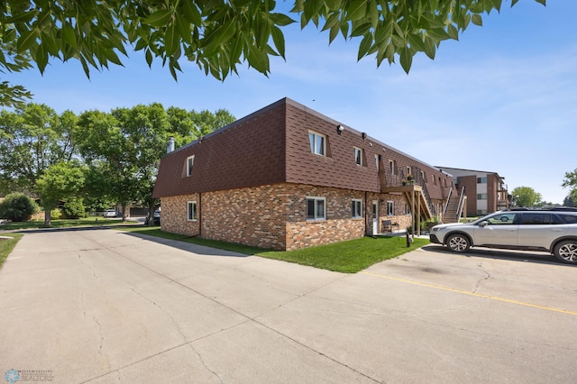 2575 Pacific Dr S Unit 301, Fargo, ND 58103 - view of home's exterior featuring brick siding, mansard roof, roof with shingles, uncovered parking, and a lawn