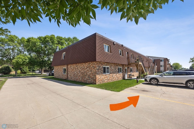 2575 Pacific Dr S Unit 301, Fargo, ND 58103 - view of side of home featuring mansard roof, brick siding, a shingled roof, uncovered parking, and stairway