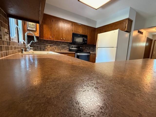 2411 Douglas St, Windom, MN 56101 - kitchen featuring freestanding refrigerator, black microwave, stainless steel electric range, decorative backsplash, and brown cabinetry