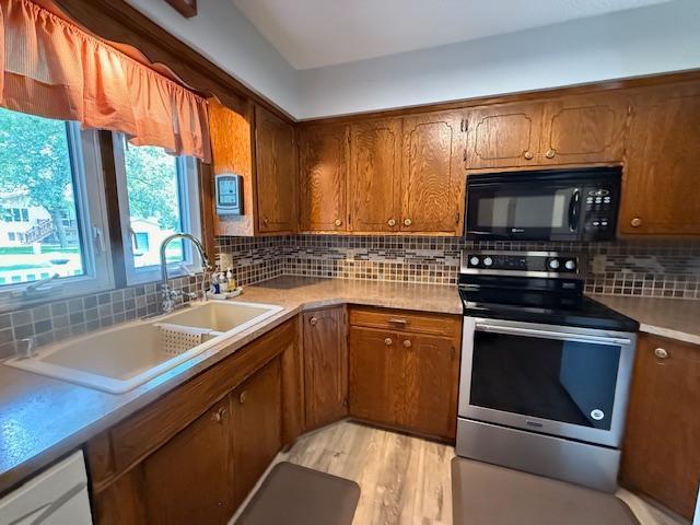 2411 Douglas St, Windom, MN 56101 - kitchen with black microwave, stainless steel range with electric stovetop, backsplash, brown cabinetry, and light wood-style floors