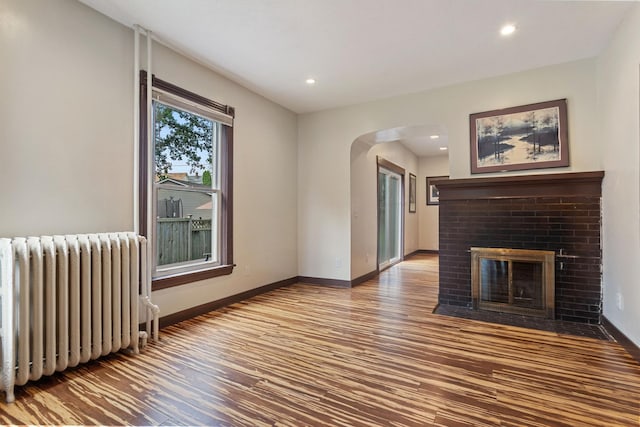 981 Bayless Ave, Saint Paul, MN 55114 - unfurnished living room with radiator heating unit, arched walkways, wood finished floors, a brick fireplace, and recessed lighting