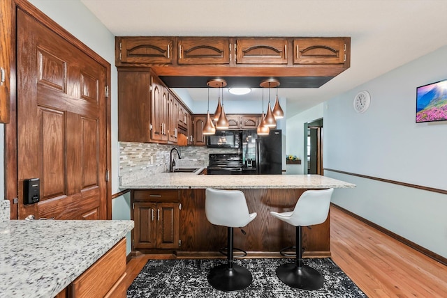 7795 Van Buren St NE, Spring Lake Park, MN 55432 - kitchen with black appliances, light wood-type flooring, backsplash, a peninsula, and decorative light fixtures