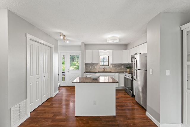 1237 Hillwind Rd NE, Fridley, MN 55432 - kitchen featuring appliances with stainless steel finishes, a kitchen island, decorative backsplash, white cabinets, and dark wood-style flooring