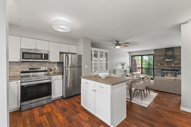 1237 Hillwind Rd NE, Fridley, MN 55432 - kitchen featuring appliances with stainless steel finishes, ceiling fan, dark wood-type flooring, and a large fireplace