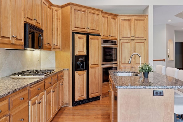 343 Waycliffe Dr N, Wayzata, MN 55391 - kitchen with appliances with stainless steel finishes, a kitchen island with sink, light wood-style flooring, light stone countertops, and tasteful backsplash