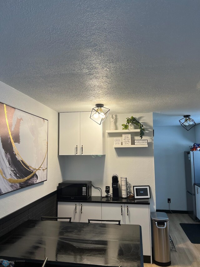 1822 7th Ave S, Fargo, ND 58103 - kitchen with black microwave, a textured ceiling, dark countertops, white cabinetry, and freestanding refrigerator