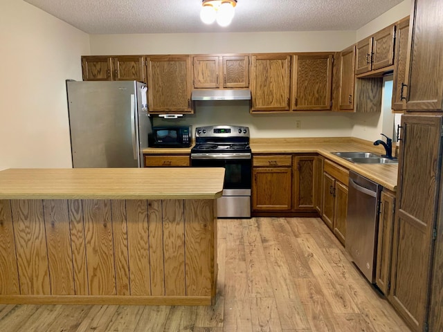 2419 25 1/2 Ave S Unit 205, Fargo, ND 58103 - kitchen featuring stainless steel appliances, under cabinet range hood, light wood-style floors, a textured ceiling, and brown cabinets