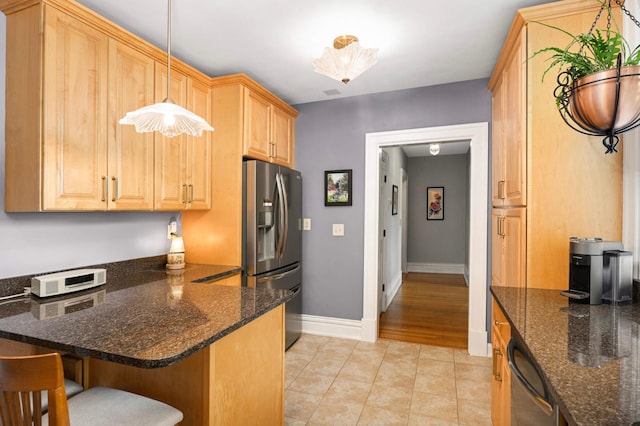 977 Portland Ave Unit 1, Saint Paul, MN 55104 - kitchen with stainless steel fridge, light tile patterned floors, a breakfast bar area, a peninsula, and dark stone countertops