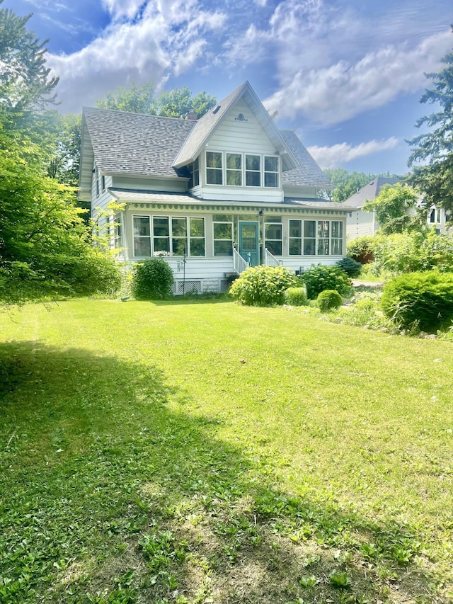 410 10th St SW, Willmar, MN 56201 - back of house featuring a sunroom, a shingled roof, and a lawn