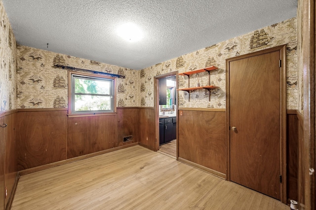 6121 Trinity Dr NE, Fridley, MN 55432 - empty room featuring wainscoting, a textured ceiling, wallpapered walls, and light wood-style floors