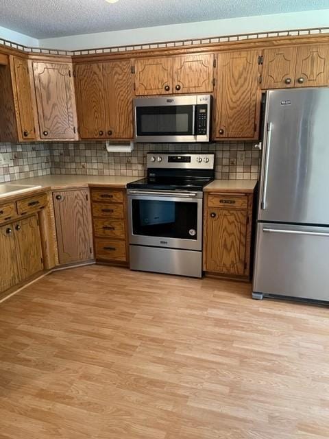 324 7th St, Windom, MN 56101 - kitchen with stainless steel appliances, light wood-type flooring, brown cabinets, backsplash, and a textured ceiling