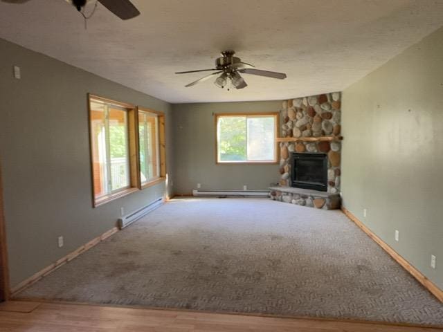 7300 County Road 8 NE, Longville, MN 56655 - unfurnished living room featuring ceiling fan, a baseboard radiator, a stone fireplace, and wood finished floors