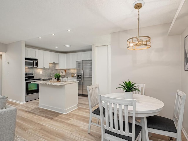 1181 Yuma Ln N, Plymouth, MN 55447 - kitchen featuring appliances with stainless steel finishes, decorative backsplash, light wood finished floors, a chandelier, and a center island